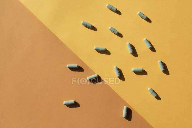 Scattered green capsules against a yellow and brown background — Stock Photo