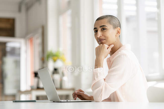Улыбающаяся деловая женщина за ноутбуком в офисе на чердаке — стоковое фото