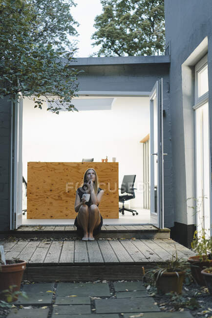 Femme d'affaires assise dans une porte de bureau ouverte, tenant une tasse de café — Photo de stock