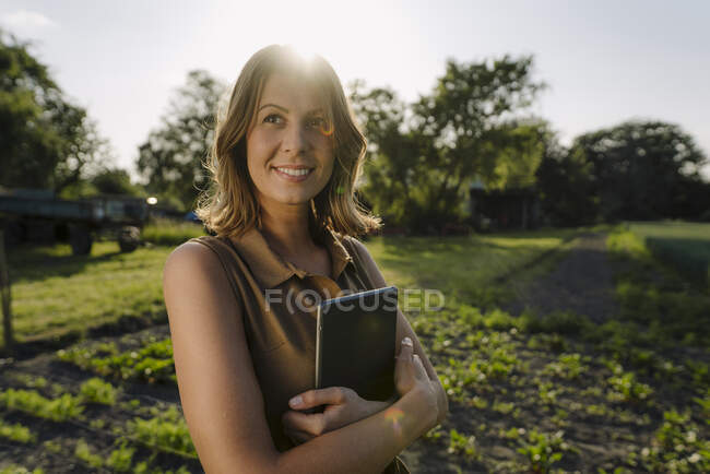 Mujer joven sonriente sosteniendo la tableta en una granja en el campo — Stock Photo
