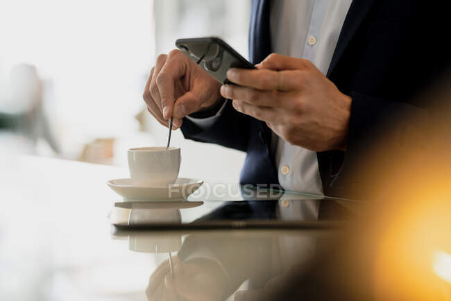 Nahaufnahme eines männlichen Profis, der sein Smartphone benutzt, während er im Café Kaffee auf dem Tresen mixt — Stockfoto