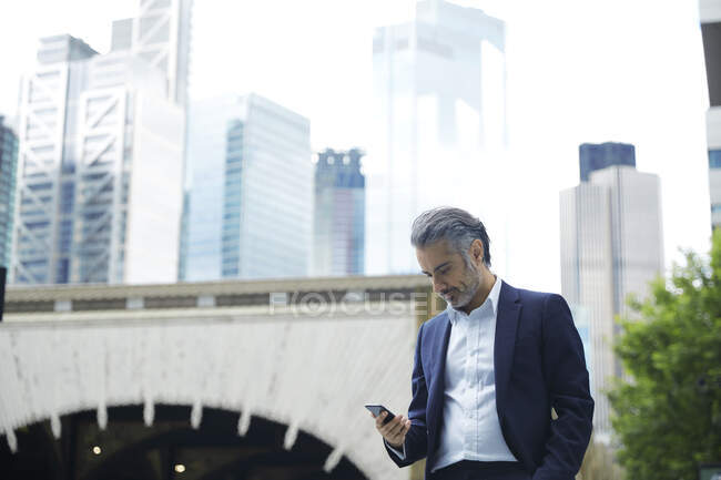 Hombre de negocios mirando el teléfono inteligente en la ciudad - foto de stock