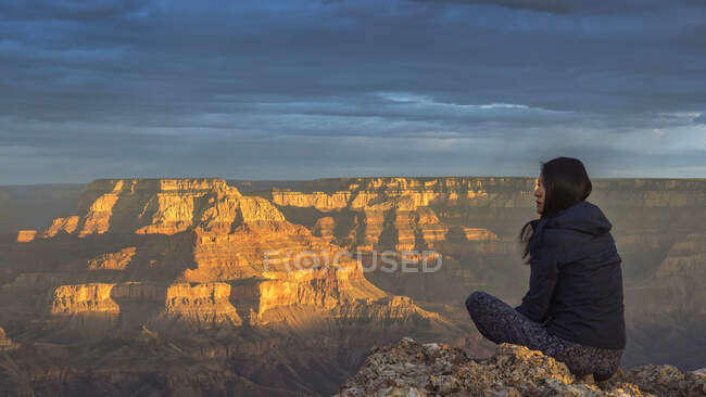 États-Unis, Arizona, Vue arrière d'une femme assise sur un rocher au Grand Canyon au coucher du soleil — Photo de stock