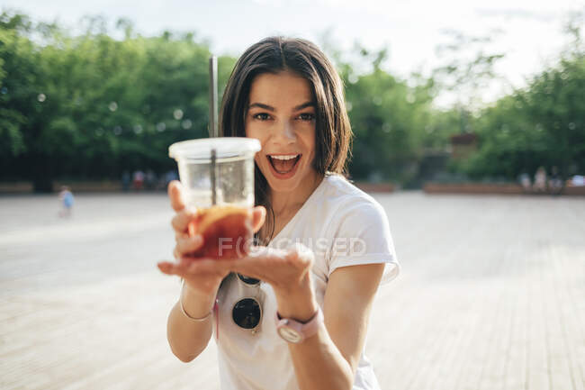Cheerful young woman with mouth open holding soft drink cup while standing in park — Stock Photo