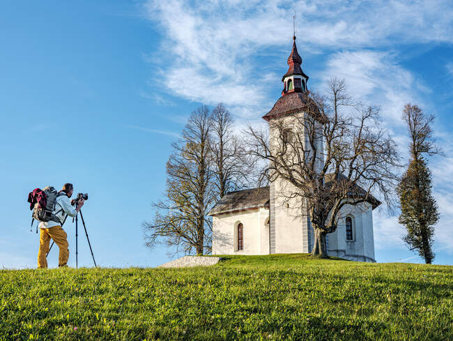 Slovenia, Alta Carniola, Comune di Skofja Loka, Uomo che fotografa la Chiesa di San Tommaso in autunno — Foto stock