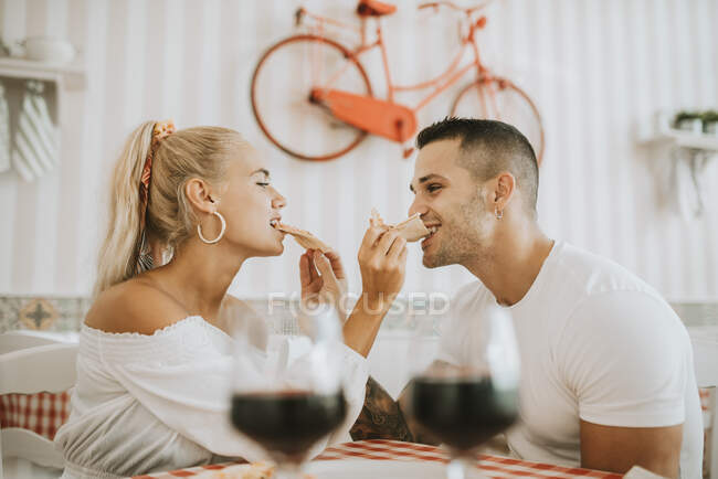 Loving young couple feeding pizza to each other in restaurant — Stock Photo