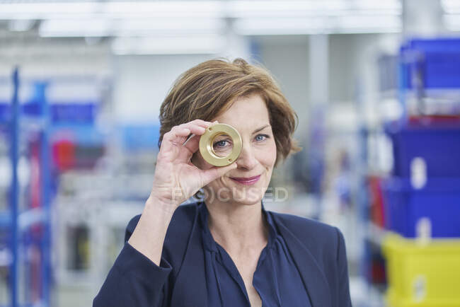 Confident female manager looking through brass object in factory — Stock Photo