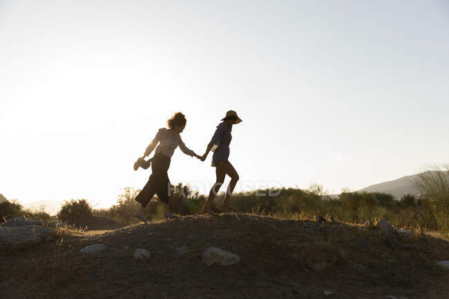 Друзья-женщины держатся за руки, гуляя по холму в сельской местности — стоковое фото