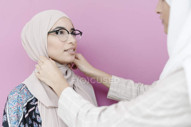 Мусульманская девушка настраивает платок для сестры на фиолетовый фон — стоковое фото