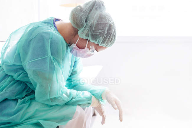 Traurige Ärztin in Schutzkleidung sitzt im Krankenhaus gegen Fenster — Stockfoto