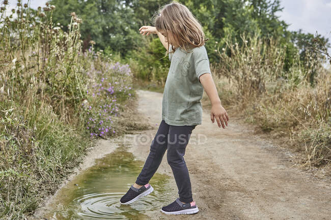 Fille jouer avec la flaque d'eau tout en se tenant sur la route de terre — Photo de stock
