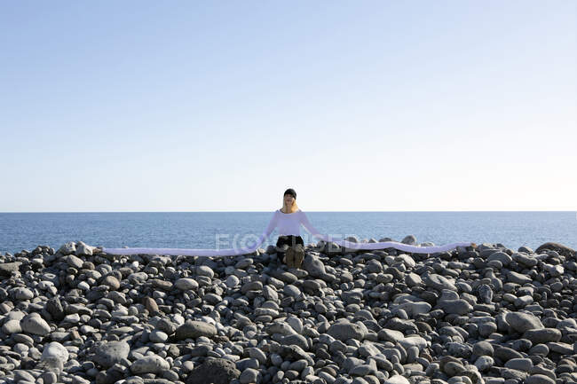 Woman with artificial long hands sitting on pebbles at beach against clear sky — Foto stock