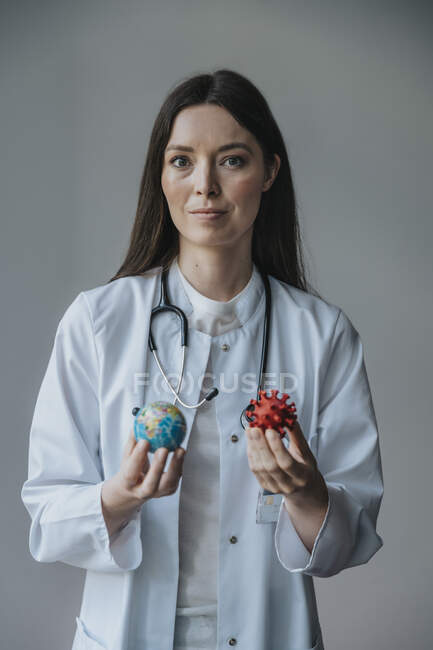 Серйозна жінка - лікар, що тримає модель земної кулі й біологічних клітин проти стінки. — стокове фото