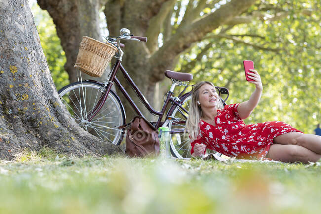 Woman taking selfie through smart phone while reclining in public park — Stock Photo