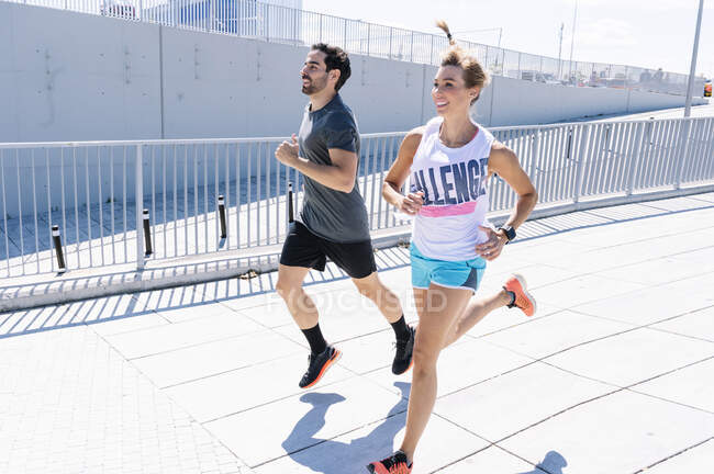 Glückliches Paar joggt bei sonnigem Wetter auf der Stadtstraße — Stockfoto