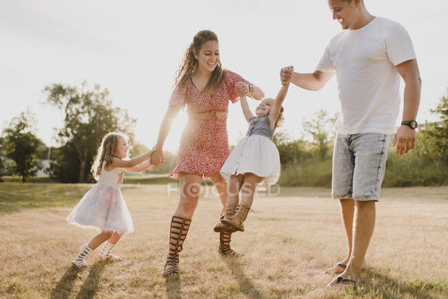 Padres felices jugando con dos hijas en un prado - foto de stock
