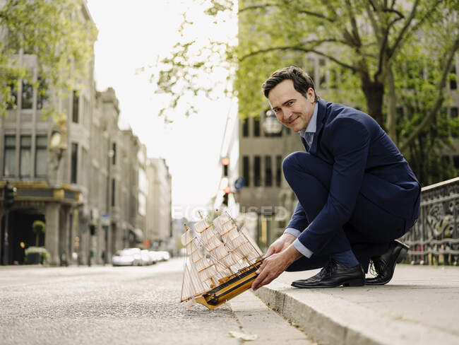 Smiling mature businessman placing model sailing ship on city street — Stock Photo