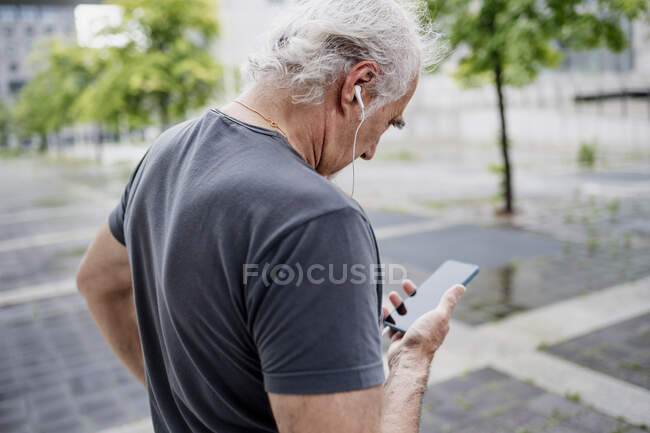 Close-up of senior man using smart phone listening music while standing outdoors — Foto stock