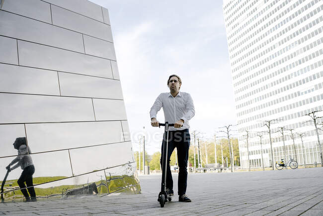 Empresário com pontapé scooter refletido na fachada do edifício — Fotografia de Stock