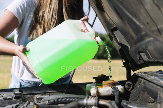 Мидсекция женщины в дороге выливает охладитель в двигатель в солнечный день — стоковое фото