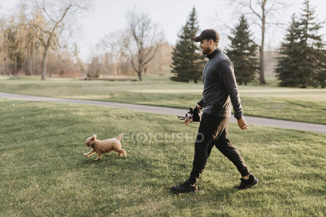 Hombre adulto medio con caniche caminando en terreno herboso en el parque - foto de stock