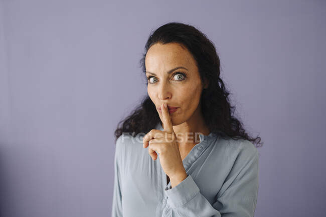 Gros plan de la femme adulte moyenne avec doigt sur les lèvres sur fond violet — Photo de stock