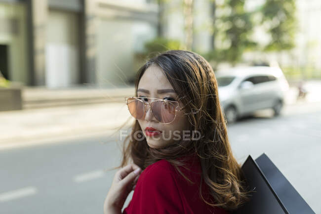 Close-up of confident woman wearing sunglasses carrying shopping bag on street in city — Stock Photo