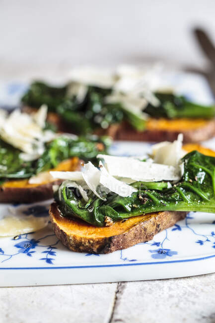 Toasted slices of sweet potato with spinach and parmesan cheese topping — Stock Photo