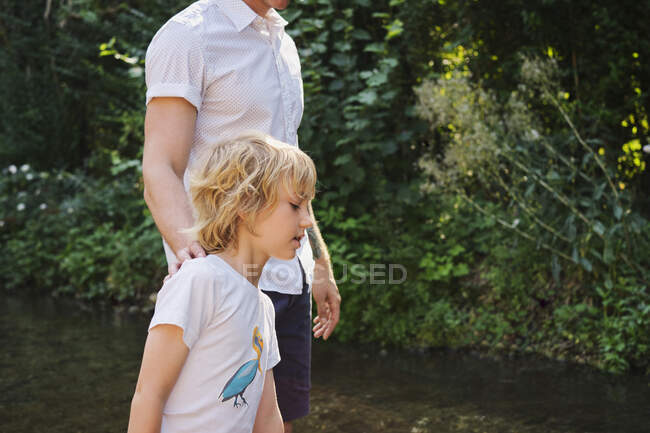 Padre e hijo caminando en arroyo durante el día soleado en el bosque - foto de stock