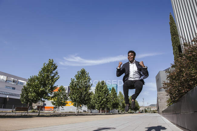 Fröhlicher männlicher Profi springt bei sonnigem Wetter auf Fußweg vor blauem Himmel in der Stadt — Stockfoto
