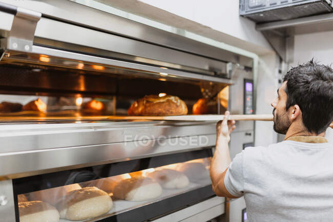 Пекарь печет хлеб в духовке в пекарне — стоковое фото