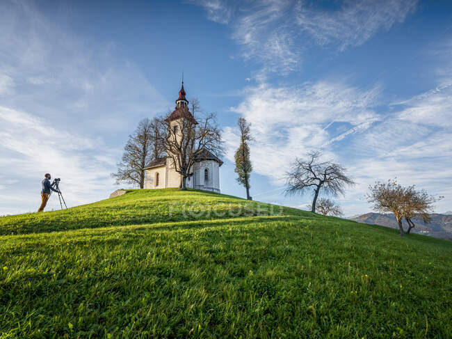 Slovenia, Upper Carniola, Municipality of Skofja Loka, Man photographing Saint Thomass Church in autumn — Stock Photo