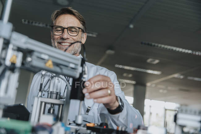 Sorridente uomo maturo indossa occhiali esaminando attrezzature in laboratorio — Foto stock
