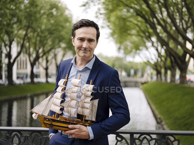 Porträt eines selbstbewussten, reifen Geschäftsmannes, der ein Modell eines Segelschiffs auf einer Brücke hält — Stockfoto