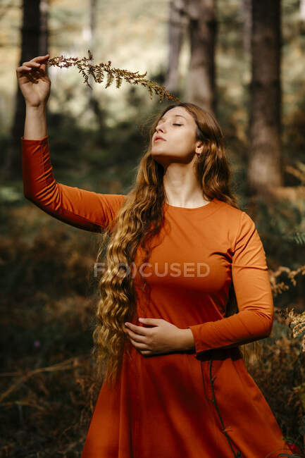 Belle femme avec les yeux fermés tenant des feuilles tout en se tenant dans les bois — Photo de stock