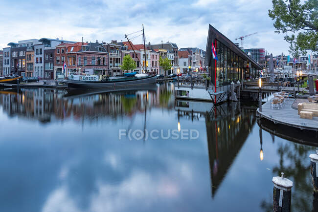 Países Bajos, Holanda Meridional, Leiden, Edificios que reflejan el canal del río Oude Rijn al atardecer - foto de stock