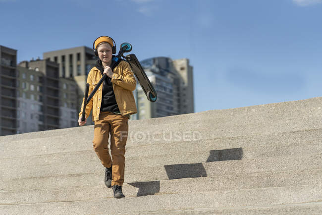 Boy carrying push scooter while moving down on steps against blue sky — Stock Photo