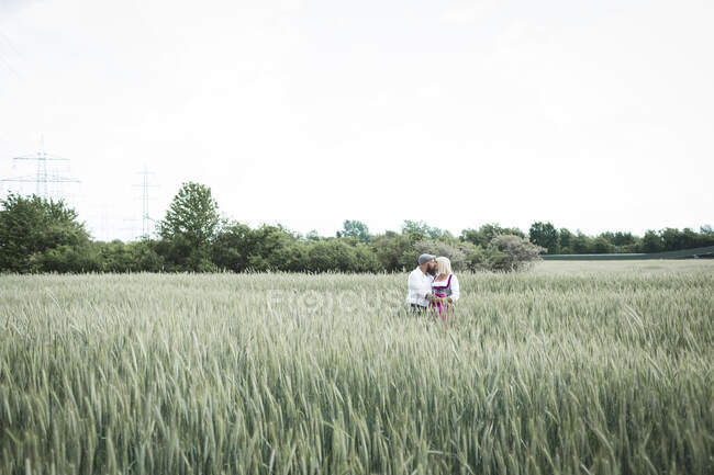 Зрелая пара целуется, стоя среди растений на фоне ясного неба — стоковое фото