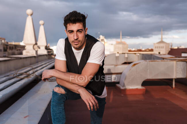 Красивый молодой человек, стоящий на заброшенной террасе здания против облачного неба в городе — стоковое фото