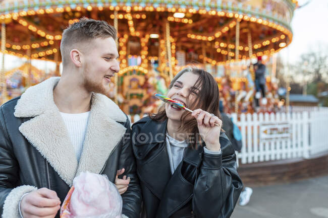 Felice uomo guardando fidanzata mangiare lecca-lecca al parco divertimenti — Foto stock