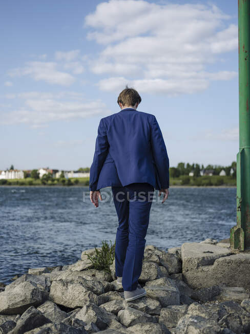Empresário vestindo terno andando sobre pedras na margem do rio Reno contra o céu — Fotografia de Stock