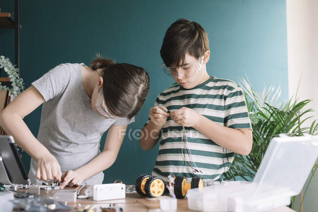 Frères et sœurs faisant jouet robotisé sur la table à la maison — Photo de stock