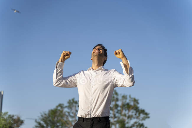 Emocionado hombre de negocios haciendo gestos mientras estaba de pie contra el cielo azul claro - foto de stock