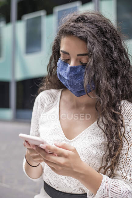Gros plan d'une jeune femme portant un masque facial à l'aide d'un téléphone portable alors qu'elle se tenait en ville — Photo de stock
