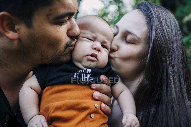 Jóvenes padres besando bebé niño - foto de stock