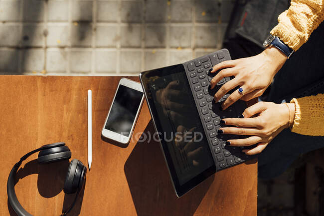 Руки студентки, які друкують на цифровій клавіатурі планшетів, сидячи в тротуарному кафе в місті — стокове фото