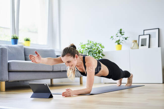 Donna che estende il braccio durante la posa tavola durante l'apprendimento esercizio su internet attraverso tablet PC — Foto stock