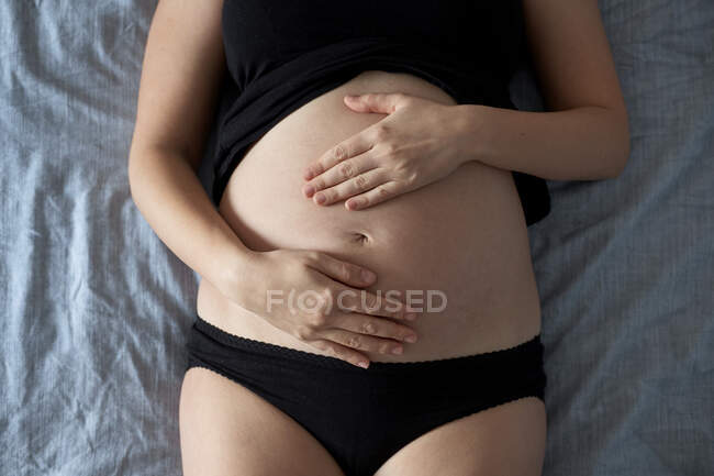 Schwangere berührt Bauch, während sie zu Hause im Bett liegt — Stockfoto