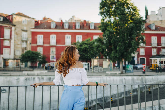 Giovane donna che distoglie lo sguardo mentre si appoggia sulla ringhiera ad Alfama, Lisbona, Portogallo — Foto stock