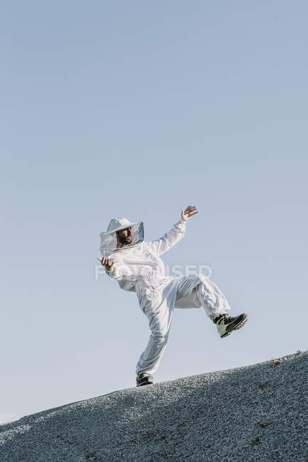 Hombre con un vestido de apicultor cayendo en una colina - foto de stock
